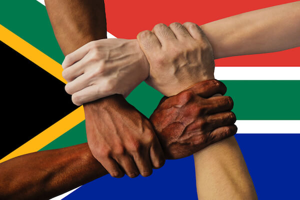 Multicultural South Africa - hands of different skin colour in front of South African flag