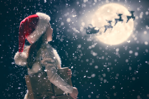 Girl looking at Santa and reindeers in snowy sky